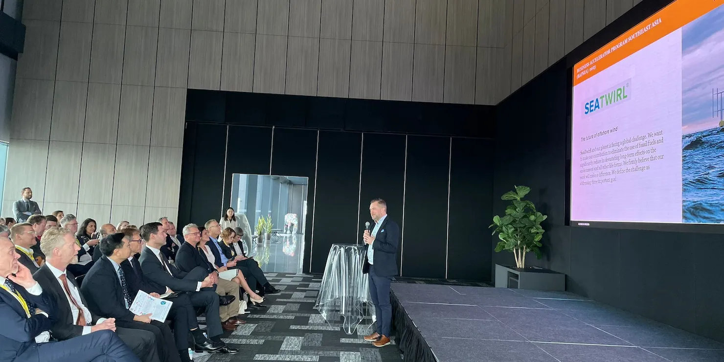 Konferenssal med sittande publik och en talare på scenen bredvid en skärm som visar en SeaTwirl-bild