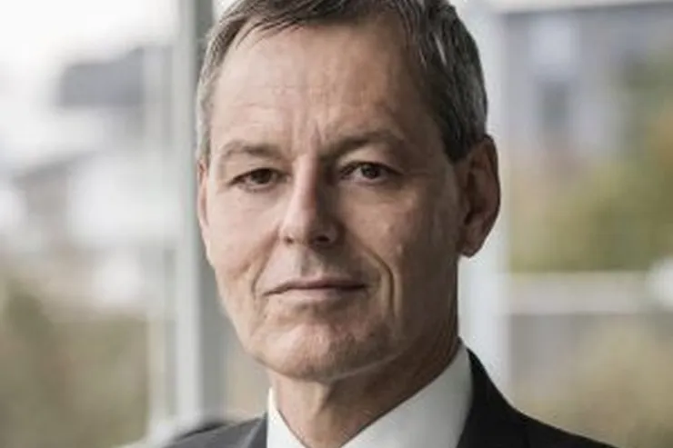 Jens Tommerup i mörk kostym och randig slips framför ett fönster