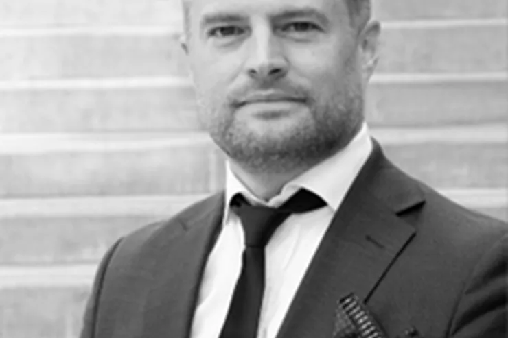 Svartvitt porträtt av Johan Sandberg i kostym och slips framför en trappa