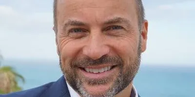 Peter Laurits leende i blå kavaj med havet bakom sig