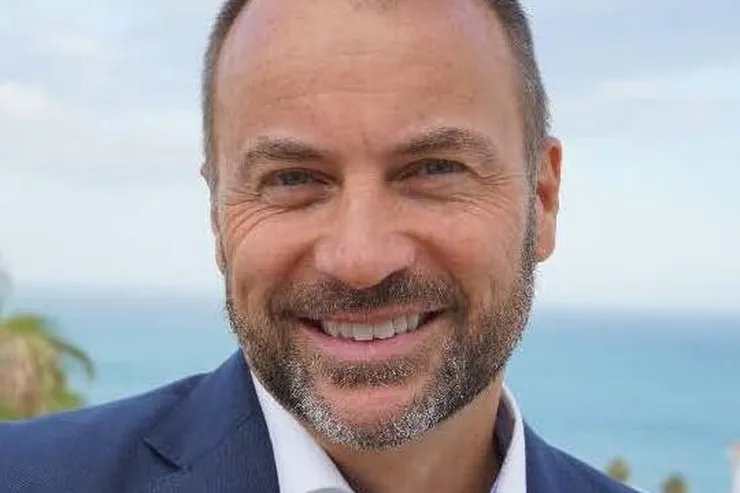 Peter Laurits leende i blå kavaj med havet bakom sig