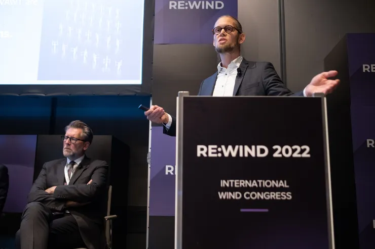 En talare vid en talarstol märkt Re:Wind 2022 International Wind Congress, med en annan paneldeltagare sittande bakom