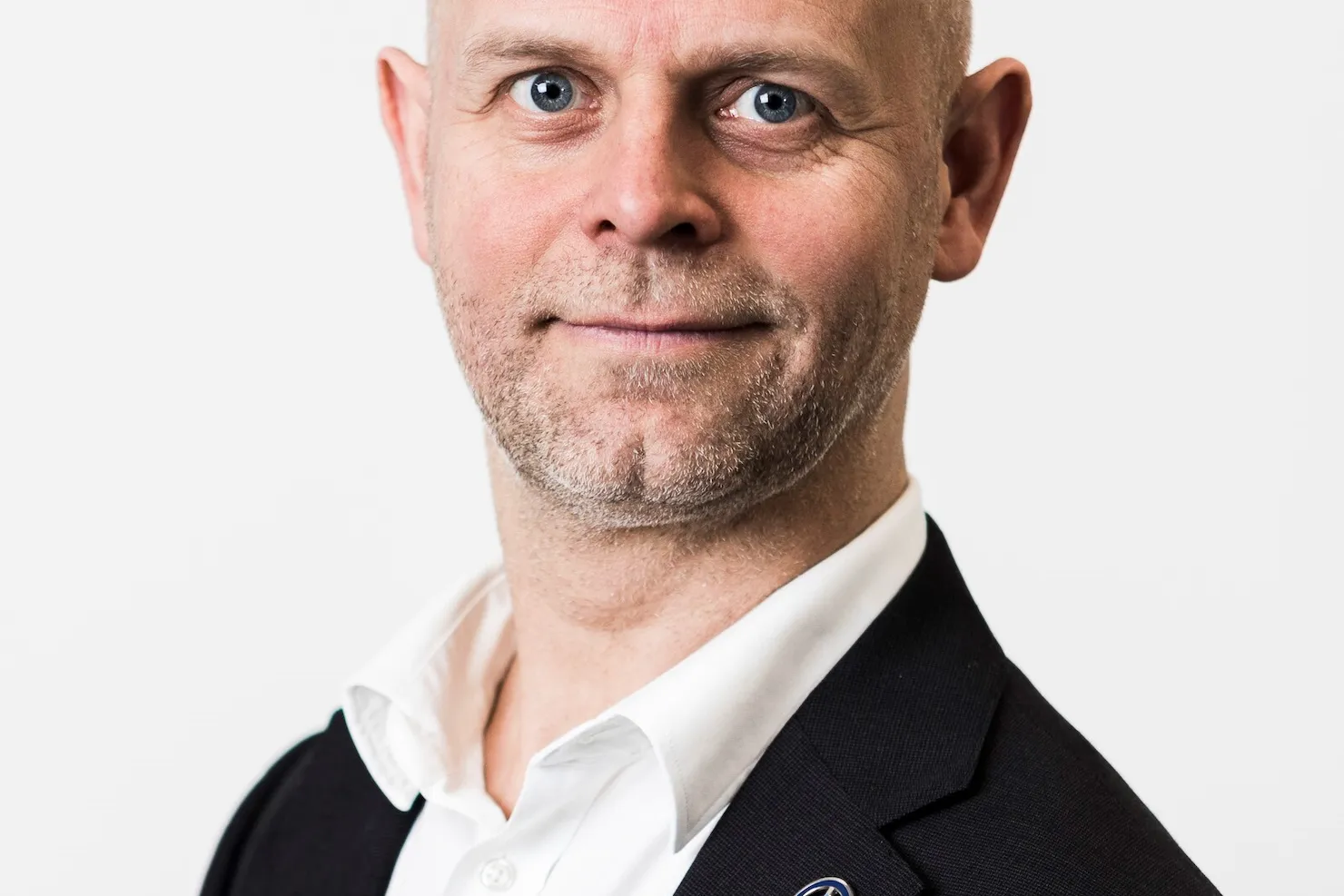 Fredrik Östbye i svart kavaj och vit skjorta mot ljusgrå bakgrund