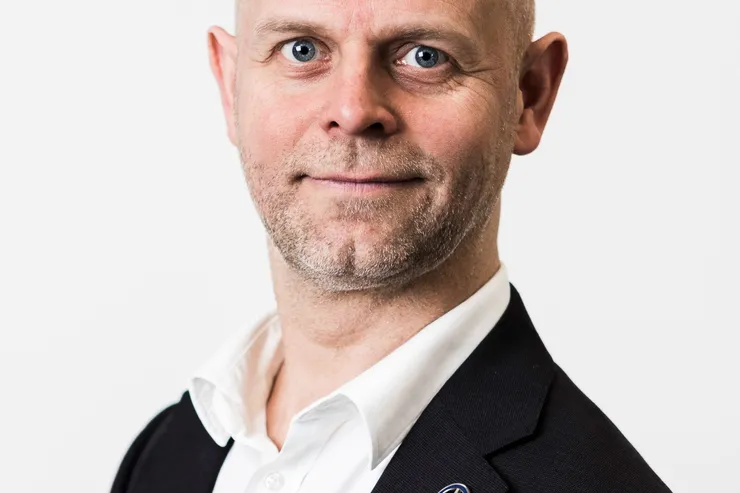 Fredrik Östbye i svart kavaj och vit skjorta mot ljusgrå bakgrund