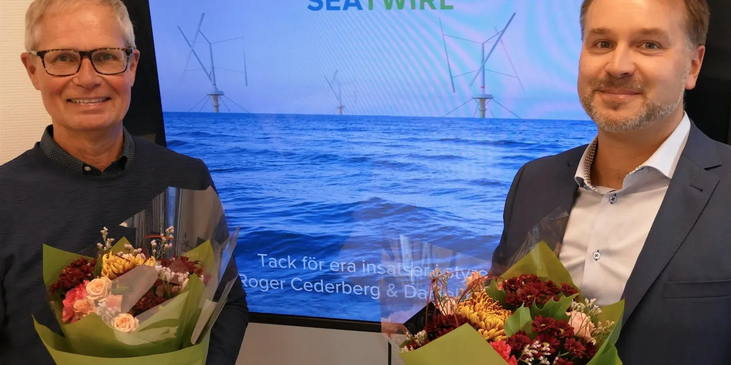 Två män med varsin blombukett framför en skärm med texten »Tack för era insatser Roger Cederberg & Daniel Ehrnberg«