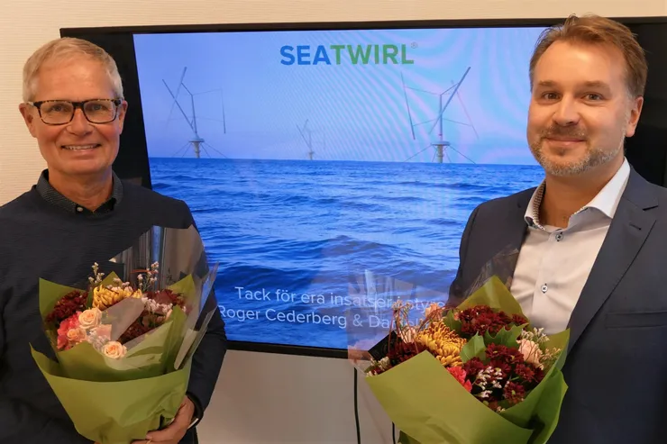 Två män med varsin blombukett framför en skärm med texten »Tack för era insatser Roger Cederberg & Daniel Ehrnberg«