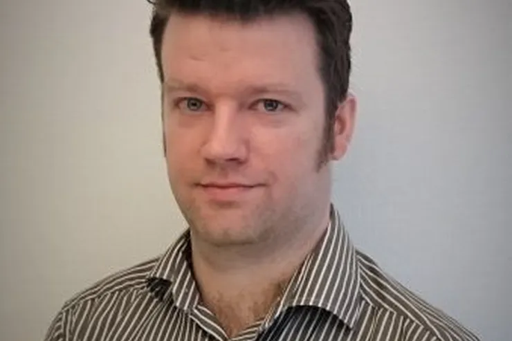 Erik Steinholtz i randig skjorta mot en grå vägg