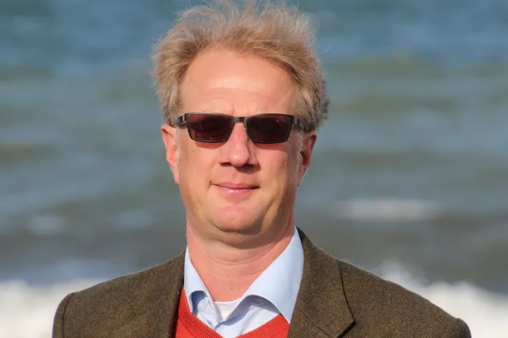 Martin i solglasögon, tweedkavaj och röd tröja med havet bakom sig