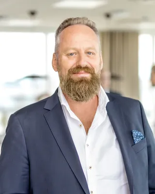 Man med fylligt rödgrått skägg i mörkblå kavaj och vit skjorta, i ett ljust kontorslandskap